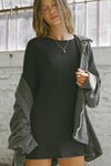 Front view model posing in the relaxed fit black modal Cowl Back Long Sleeve Mini Dress \with a crew neckline, A-line silhouette, adjustable straps at the center back and neck and an open back with a draped cowl detail.