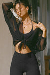 Front view of model posing in the sheer, relaxed fit black polka dot lace Knotted Crop Cardigan long sleeve top with an open front, and adjustable front tie that can be knotted at the center for a customizable fit and shape.