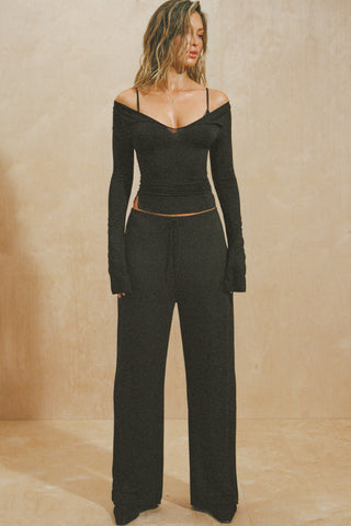 Full body front view of model posing in the fitted black modal Notched V Neck Long Sleeve top with a deep notched V-neckline, extra long sleeves and small side slits at the hem