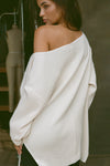 Back view of model posing in the relaxed fit natural luxe knit Off Shoulder Tunic with a wide off-the-shoulder neckline and asymmetrical hem