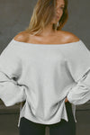 Front view of model posing in the relaxed fit pearl grey luxe knit Off Shoulder Tunic with a wide off-the-shoulder neckline and asymmetrical hem