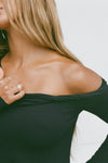 Close up detail front view of model posing in the fitted black rib Off Shoulder Twist Long Sleeve top asymmetrical neckline with a twist detail and off-shoulder design