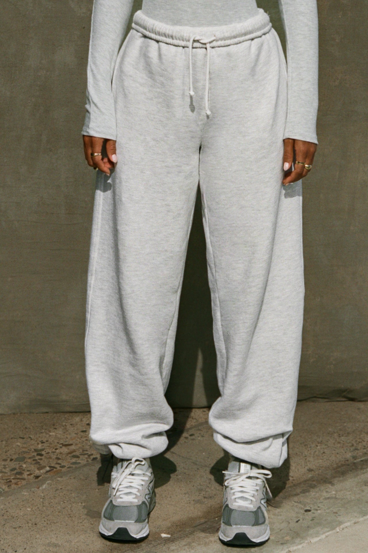Front view of model from the waist down posing in the relaxed fit pearl grey french terry Oversized Straight Leg Jogger with an elastic waistband, hidden drawstring, pocket details. and adjustable cinching at the ankle cuffs