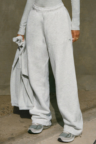 Front view of model from the waist down posing in the relaxed fit pearl grey french terry Oversized Straight Leg Jogger with an elastic waistband, hidden drawstring, pocket details. and adjustable cinching at the ankle cuffs