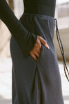 Close up detail side view of model from the waist down posing in the relaxed fit midnight luxe knit Relaxed Tapered Pant with a tapered leg, side pockets, hidden adjustable drawstring and subtle pleating at the sides for added shape and dimension.