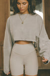 Front view of model posing in the cropped relaxed fit sandstone cotton Slouchy Crop Long Sleeve top with a crew neckline, dropped shoulders and oversized sleeves