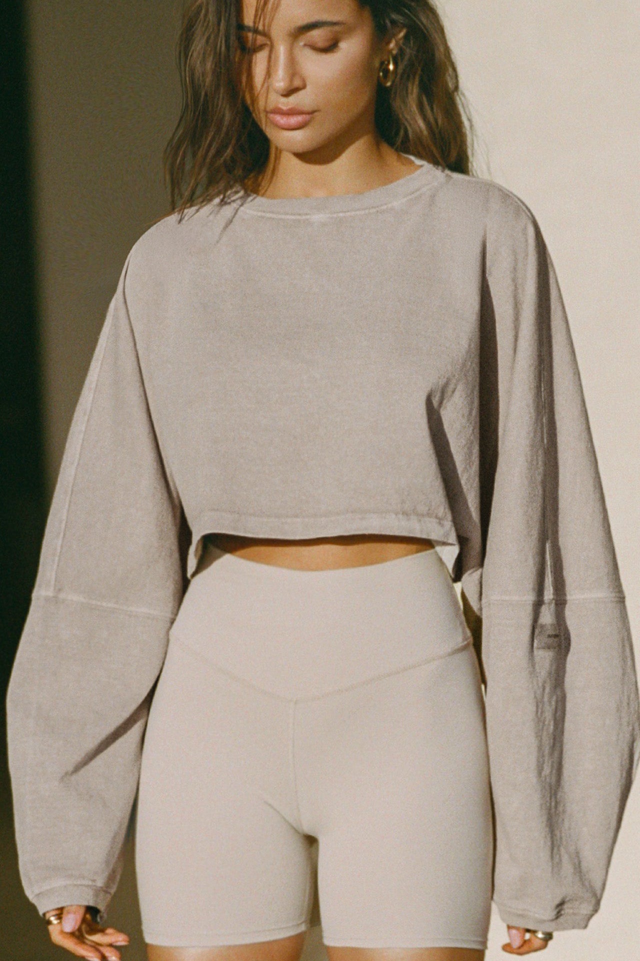 Front view of model posing in the cropped relaxed fit sandstone cotton Slouchy Crop Long Sleeve top with a crew neckline, dropped shoulders and oversized sleeves