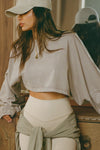 Side view of model posing in the cropped relaxed fit sandstone cotton Slouchy Crop Long Sleeve top with a crew neckline, dropped shoulders and oversized sleeves