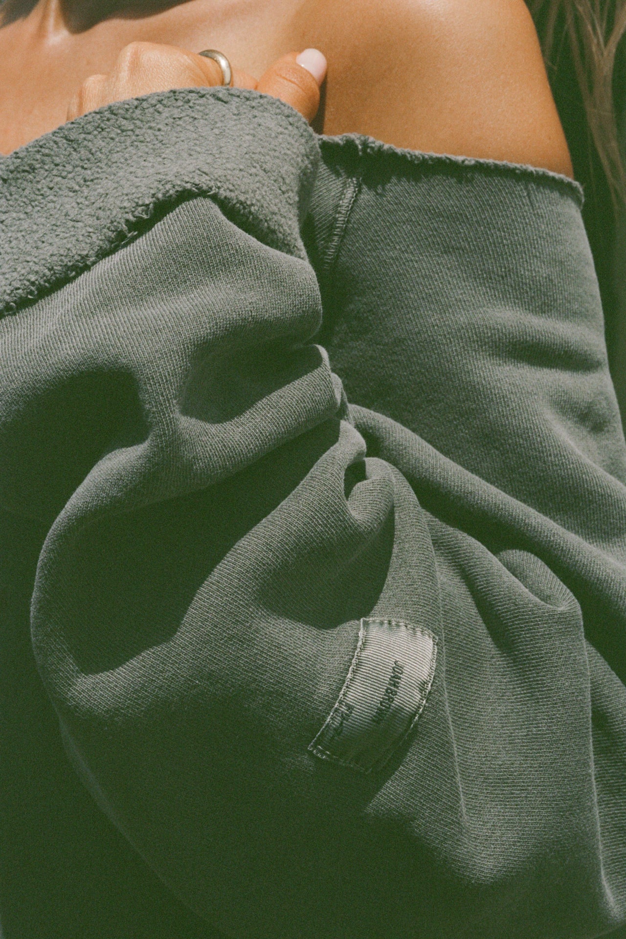 Close up detail view of  the oversized washed sage french terry Slouchy Pullover Sweatshirt with a wide, off-the-shoulder neckline and a JOAH BROWN logo patch on the right sleeve