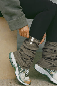 Close up side view of model adjusting the slouchy, pull on army luxe knit Leg Warmers that can be worn pulled up on scrunched down