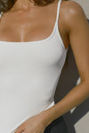 Close up detail front view of model posing in the soft and stretchy sueded white Smoothing Cami with a scoop neckline and thin straps