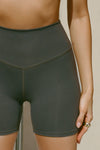 Close up detail front view of model from the waist down posing in the stretch high-waisted sueded essex 4 Inch Body Short with slimming and contouring wide waistband and 4 inch inseam.