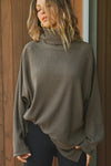 Front view of model posing in the relaxed and slouchy tunic-style army luxe knit Turtleneck Tunic with dropped shoulders, side slits and adjustable ties for a customized shape