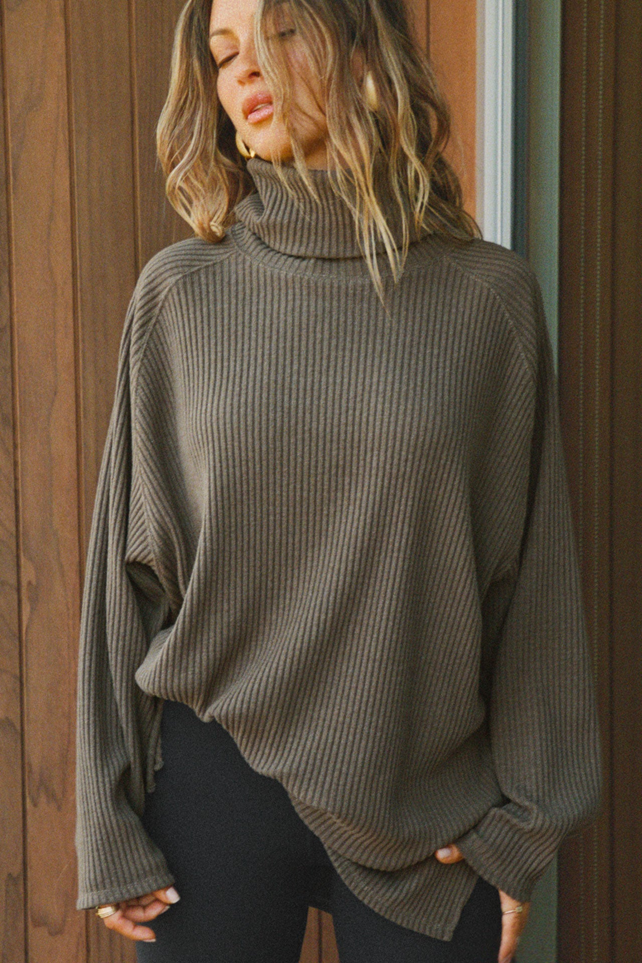 Front view of model posing in the relaxed and slouchy tunic-style army luxe knit Turtleneck Tunic with dropped shoulders, side slits and adjustable ties for a customized shape
