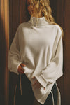 Front view of model posing in the relaxed and slouchy tunic-style natural luxe knit Turtleneck Tunic with dropped shoulders, side slits and adjustable ties for a customized shape
