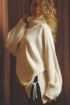 Side view of model posing in the relaxed and slouchy tunic-style natural luxe knit Turtleneck Tunic with dropped shoulders, side slits and adjustable ties for a customized shape