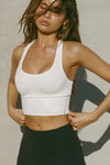 Front view of model posing in the fitted stretchy cropped white  flexrib Varsity Tank Bra with a scoop neckline