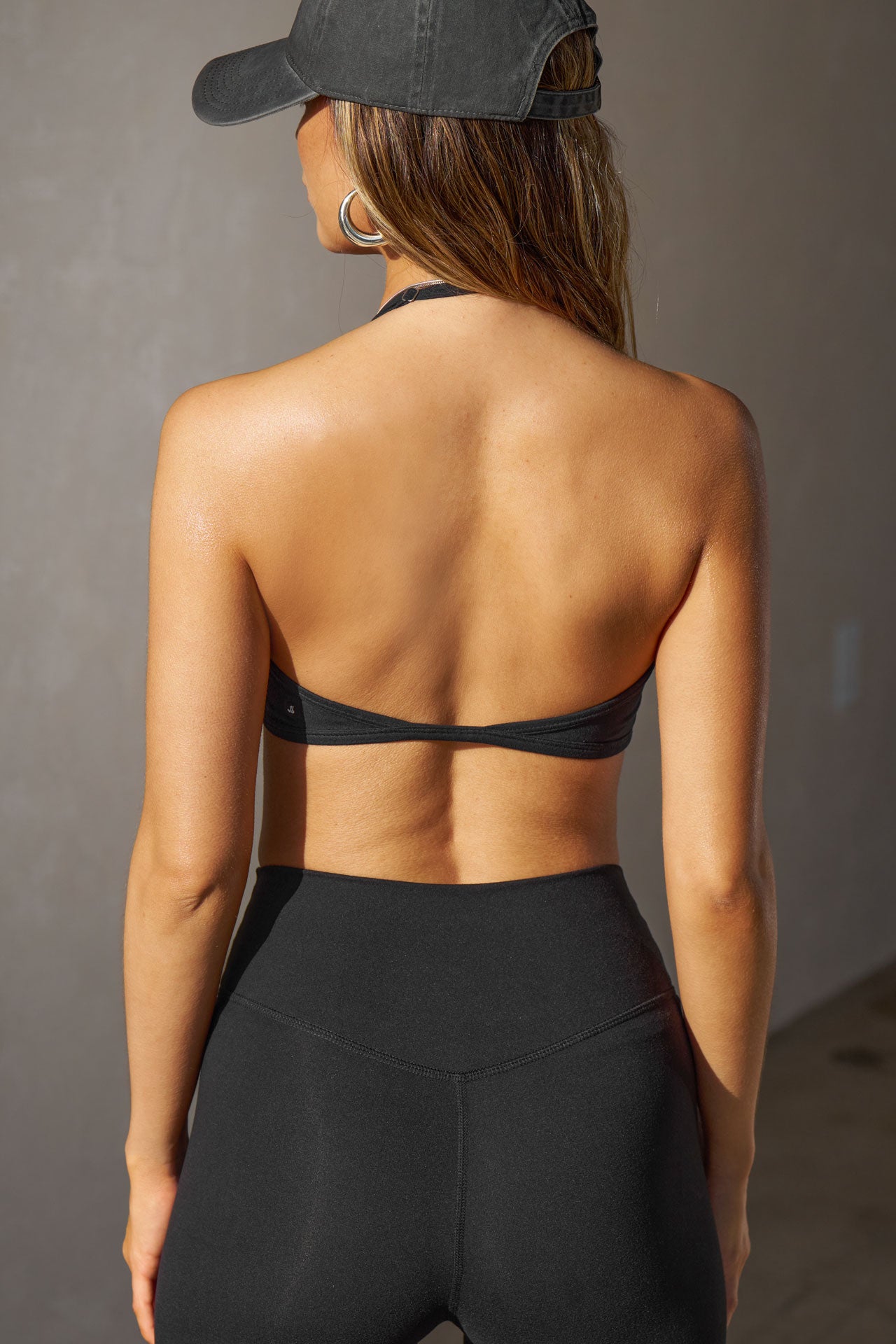 Back view of model posing in the sueded onyx Halter Scoop Bra top with an adjustable halter neck strap and open back
