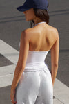 Back view of model posing outside in the street in the fitted and smoothing sueded white Halter Scoop Tank with a scoop neckline, open back and narrow, adjustable neck strap