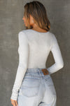 Back view of model posing in the fitted pearl grey rib Henley Long Sleeve with a notch in the scoop neckline
