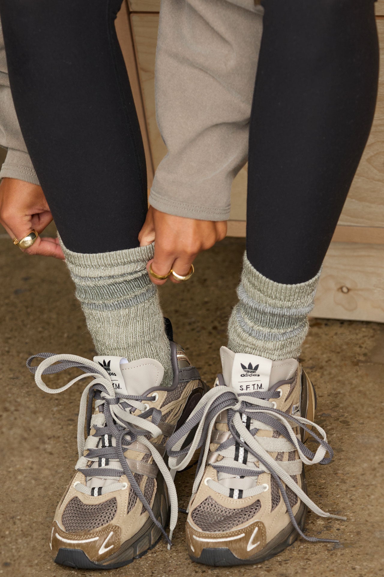 Close up front view of model adjusting the crew-style ribbed and soft heathered olive Merino Stripe Sock