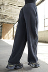Side view of model from the waist down posing in the relaxed fit midnight luxe knit Relaxed Tapered Pant with a tapered leg, side pockets, hidden adjustable drawstring and subtle pleating at the sides for added shape and dimension.
