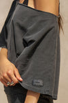 Close up detail side view of model posing in the relaxed fit and boxy washed black cotton Off Shoulder Tee with a wide scoop neckline that can be worn off the shoulders.