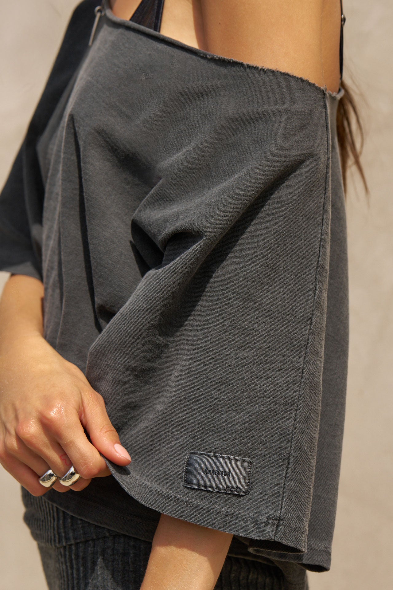 Close up detail side view of model posing in the relaxed fit and boxy washed black cotton Off Shoulder Tee with a wide scoop neckline that can be worn off the shoulders.