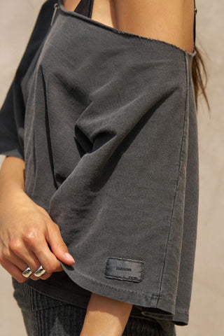 Close up detail side view of model posing in the relaxed fit and boxy washed black cotton Off Shoulder Tee with a wide scoop neckline that can be worn off the shoulders.