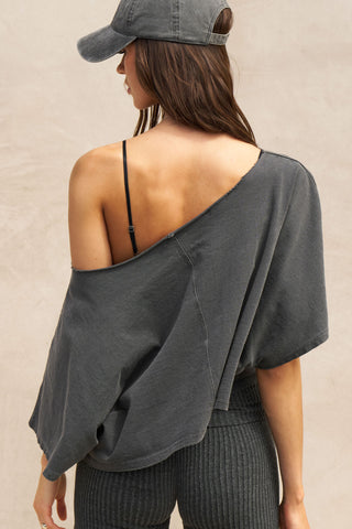Back view of model posing in the relaxed fit and boxy washed black cotton Off Shoulder Tee with a wide scoop neckline that can be worn off the shoulders.