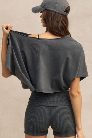 Back view of model posing in the relaxed fit and boxy washed black cotton Off Shoulder Tee with a wide scoop neckline that can be worn off the shoulders.