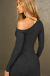 Back view of model posing in the fitted black rib Off Shoulder Twist Long Sleeve top asymmetrical neckline with a twist detail and off-shoulder design