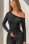 Front view of model posing in the fitted black rib Off Shoulder Twist Long Sleeve top asymmetrical neckline with a twist detail and off-shoulder design