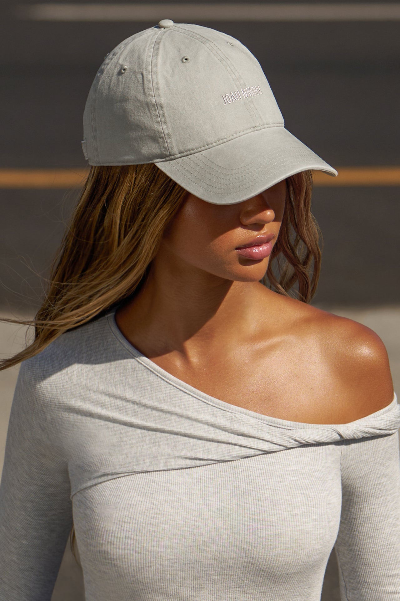 Side view of model posing in the six-panel sahara Official Cap with a curved brim and an embroidered upside down Joah Brown logo on the front