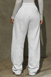 Back view of model from the waist down posing in the relaxed fit pearl grey french terry Oversized Straight Leg Jogger with an elastic waistband, hidden drawstring, pocket details. and adjustable cinching at the ankle cuffs