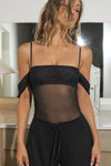 Front view of model posing in the sheer and fitted black mesh Off The Shoulder Bandeau Tank with thin straps and draped sleeves and can be worn off the shoulder or with the sleeves up