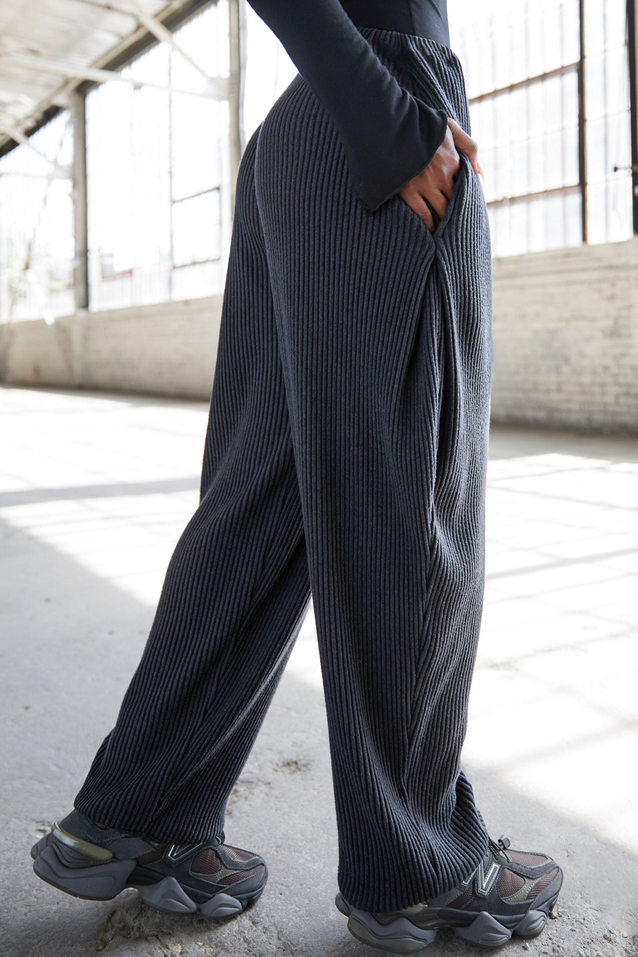 Side view of model from the waist down posing in the relaxed fit midnight luxe knit Relaxed Tapered Pant with a tapered leg, side pockets, hidden adjustable drawstring and subtle pleating at the sides for added shape and dimension.