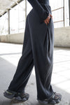 Side view of model from the waist down posing in the relaxed fit midnight luxe knit Relaxed Tapered Pant with a tapered leg, side pockets, hidden adjustable drawstring and subtle pleating at the sides for added shape and dimension.