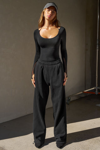 Full body front view of model posing in the fitted black flexrib Scoop Corset Long Sleeve with a scoop neckline, adjustable ties at the neck, and thumbholes in the mesh sleeves