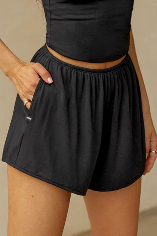 Close up front view of model from the waist down posing in the relaxed-fit fawn nylon Classic Track Short with an elastic waistband, side seam pockets, and adjustable drawcord