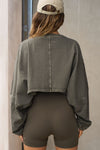 Back view of model posing in the cropped relaxed fit haze cotton Slouchy Crop Long Sleeve top with a crew neckline, dropped shoulders and oversized sleeves