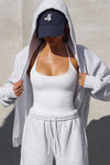 Front view of model posing outside in the fitted and smoothing sueded white Halter Scoop Tank with a scoop neckline, open back and narrow, adjustable neck strap
