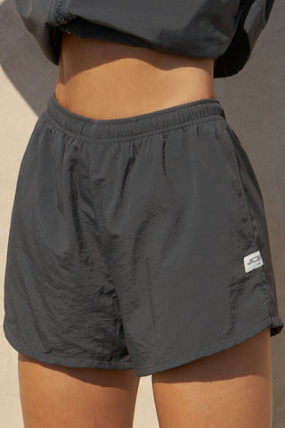 Close up front view of model from the waist down posing in the relaxed-fit jet nylon Classic Track Short with an elastic waistband, side seam pockets, and adjustable drawcord.