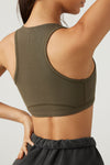 Back view of model posing in the fitted stretchy army flexrib Stitch Bra top with a racerback and stitched detailing at the bust