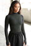 Front view of model posing in the fitted vintage black flexrib Stitch Mock Neck Long Sleeve top with tonal stitching on the front, a mock neckline and thumbholes in the cuffs