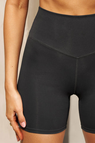 Close up detail front view of model from the waist down posing in the stretch high-waisted sueded onyx 4 Inch Body Short with slimming and contouring wide waistband and 4 inch inseam.
