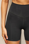 Close up detail front view of model from the waist down posing in the stretch high-waisted sueded onyx 4 Inch Body Short with slimming and contouring wide waistband and 4 inch inseam.