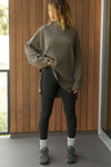 Full body front view of model posing in the relaxed and slouchy tunic-style army luxe knit Turtleneck Tunic with dropped shoulders, side slits and adjustable ties for a customized shape