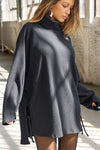 Front view of model posing in the relaxed and slouchy tunic-style midnight luxe knit Turtleneck Tunic with dropped shoulders, side slits and adjustable ties for a customized shape