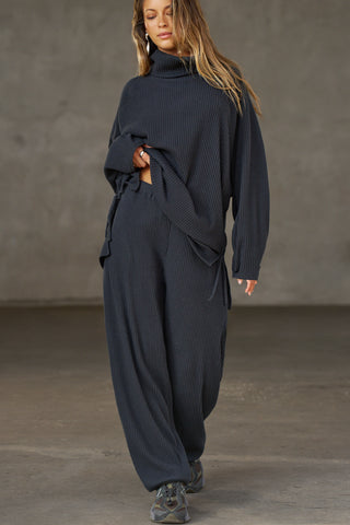 Full body front view of model posing in the relaxed fit midnight luxe knit Relaxed Tapered Pant with a tapered leg, side pockets, hidden adjustable drawstring and subtle pleating at the sides for added shape and dimension.